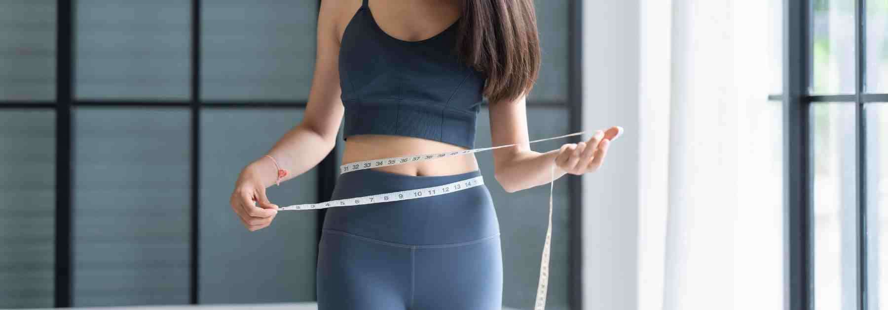 Woman measuring medical weight loss success with tape measure